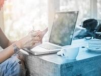 Image of a person in front of a laptop holding a smartphone Image of a person in front of a laptop holding a smartphone
