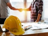 Image of yellow safety helmet on workplace desk with construction workers shaking hands