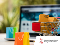 Image of a shopping trolley with boxes in it, shopping bags and a laptop in the background