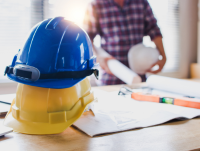 Image of construction safety helmets on table with a person holding blueprints