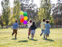 A group of children running across a park holding colourful balloons