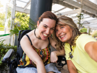 A person in a wheelchair smiling while touching heads with another person