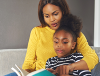 Mother and chid sat on a sofa reading a book together