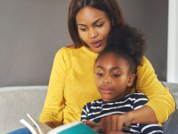Mother and chid sat on a sofa reading a book together